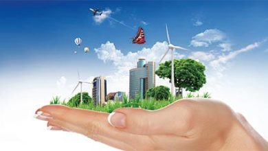 Illustration conceptuelle montrant une main ouverte soutenant une petite ville écologique. Sur la paume, on voit des immeubles modernes entourés d’espaces verts, des arbres, des éoliennes et des ballons dans le ciel. L’ensemble évoque le développement durable, les énergies renouvelables et la responsabilité environnementale dans un cadre urbain futuriste.