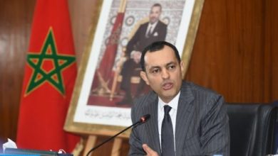 Responsable marocain s’exprimant lors d’une réunion officielle, assis devant un micro, avec le drapeau du Maroc et un portrait du Roi en arrière-plan.