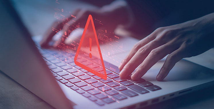 Gros plan sur des mains tapant sur un ordinateur portable, avec un symbole d’alerte rouge superposé à l’écran, illustrant un risque ou une menace en cybersécurité, comme une attaque informatique ou une intrusion dans un système.