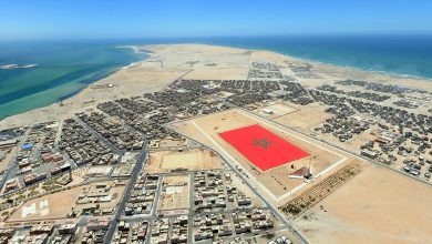 Vue aérienne de Dakhla montrant la ville entre lagune et océan Atlantique, avec une grande place arborant le drapeau marocain au cœur d’un environnement désertique.