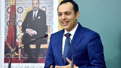 Responsable marocain s’exprimant lors d’une réunion officielle, assis devant un micro, avec le drapeau du Maroc et un portrait du Roi en arrière-plan