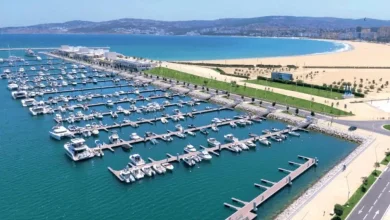 Vue aérienne d’une marina moderne au Maroc avec des bateaux amarrés, située en bord de mer près d’une plage aménagée, illustrant le développement des infrastructures touristiques et maritimes.
