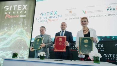 Signature officielle lors de GITEX Future Health Africa à Casablanca, avec trois responsables présentant des dossiers après un partenariat, devant un écran affichant l’événement.