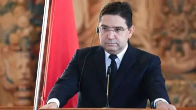 Portrait de Nasser Bourita lors d’une intervention officielle, devant un drapeau marocain, à l’occasion d’un événement diplomatique international.
