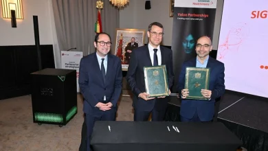 Signature d’un partenariat stratégique entre Siemens Healthineers et Mediot AI lors d’une cérémonie officielle au Maroc. Trois dirigeants en costume posent devant une table de signature, tandis que deux représentants tiennent les accords signés. À l’arrière-plan figurent le drapeau marocain, un portrait officiel du Roi Mohammed VI et les supports visuels de Siemens Healthineers, illustrant une alliance axée sur l’intelligence artificielle appliquée à la santé et aux infrastructures hospitalières en Afrique.